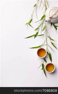 Asian food background set with green tea, cups and teapot with bamboo branches and free space for text on white background. Flat lay