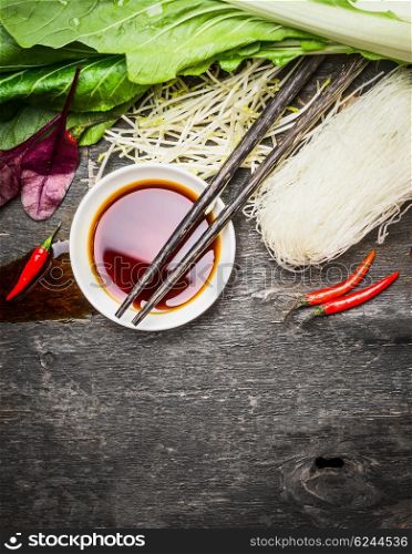 Asian food background with soy sauce, chopsticks, rice noodles and vegetables for tasty Chinese or Thai cooking, top view