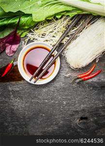 Asian food background with soy sauce, chopsticks, rice noodles and vegetables for tasty Chinese or Thai cooking, top view