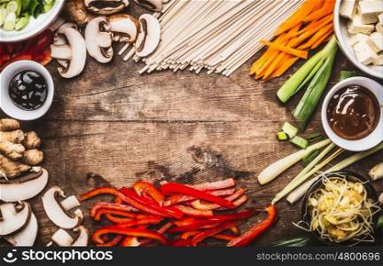 Asian food background with vegetarian cooking ingredients and chopsticks : tofu, noodles, ginger, lemongrass, cut vegetables, Sprout,green onion ,hoisin and austern sauce, top view, frame
