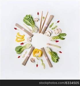 Asian food creative layout round frame on white desk background, top view. Asian cuisine ingredients with soba noodles, vegetables, spices and pak choi. Vegetarian eating and healthy nutrition concept