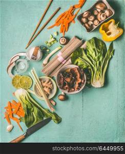 Asian food ingredients for tasty vegetarian cooking and eating: noodles, pak choy, chopped vegetables, chopsticks, Mu Err mushrooms, lemon grass, coconut, lime and spices, top view