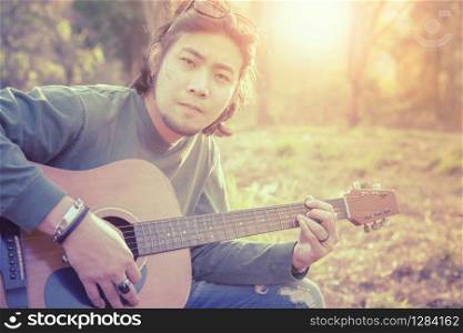 asian freelance musician playing folk guitar outdoor against beautiful sun light