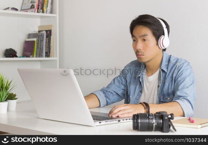 Asian Freelance Videographer in Denim or Jeans Shirt Checking Multimedia Sound by Laptop in Home Office. Freelance Videographer working with technology