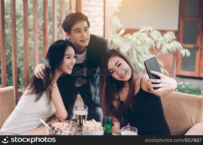 Asian friends smiling and taking selfie in restaurant.