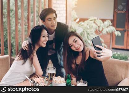 Asian friends smiling and taking selfie in restaurant.