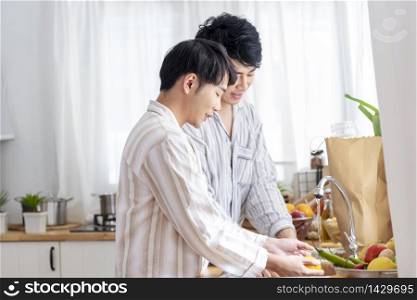 Asian gay couple homosexual cooking together in the kitchen prepare fresh vegetable make organic salad healthy food. Asian people happy time smile, laugh in kitchen. LGBTQ relation lifestyle concept