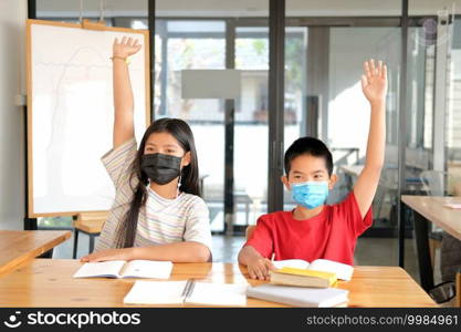 asian girl boy student wearing face mask studying raising hand in classroom. learning education at school