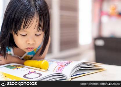 Asian girl child reading interactive book in living room at home as home schooling while city lockdown because of covid-19 pandemic across the world. Home Scholling prepare for Preschool concept.