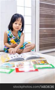 Asian girl child reading interactive book in living room at home as home schooling while city lockdown because of covid-19 pandemic across the world. Home Scholling prepare for Preschool concept.