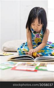 Asian girl child reading interactive book in living room at home as home schooling while city lockdown because of covid-19 pandemic across the world. Home Schooling prepare for Preschool concept.