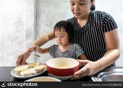 Asian girl cooking egg tart bakery with her mom, housework for child make executive function for kid. Houseworking food lifstyle and family concept.