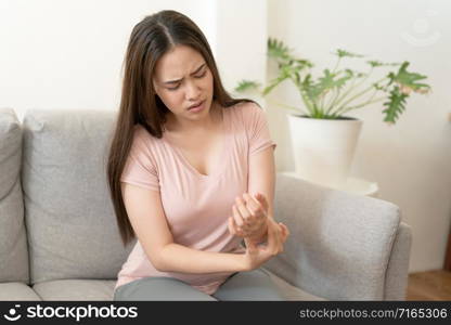 Asian girl having Wrist Pain sitting on sofa at home. young girl has pain arthritis, Health and illness concepts