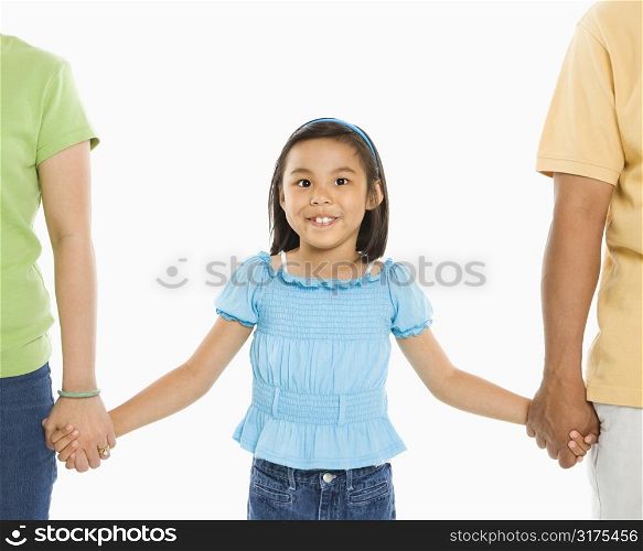 Asian girl holding hands with mother and father in front of white background.
