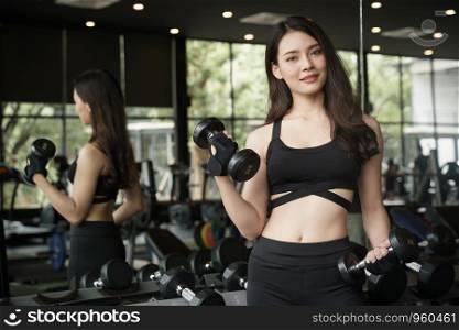 Asian girl is standing holding a dumbbell and smiling in fitness a mirrored room, Healthy concept