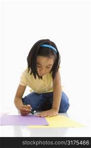 Asian girl sitting on floor coloring on paper.