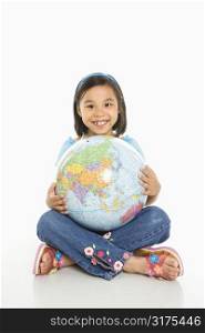 Asian girl sitting on floor holding Earth globe in her lap.