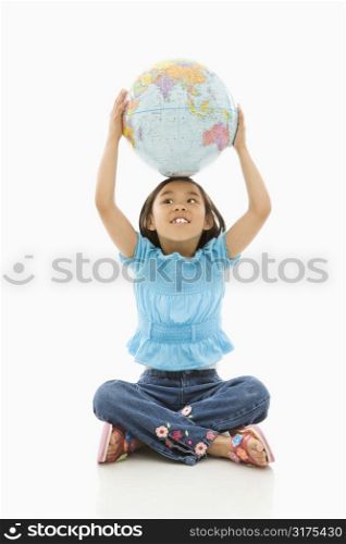 Asian girl sitting on floor holding Earth globe over her head.