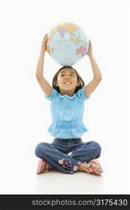 Asian girl sitting on floor holding Earth globe over her head.