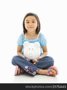 Asian girl sitting on floor holding piggybank.