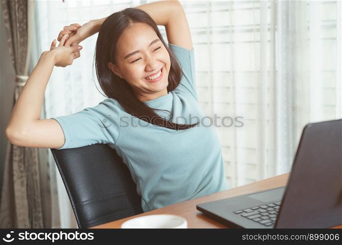 Asian girl sitting working with laptop for long time. women is tired from working, stretching up, relaxed and smiling
