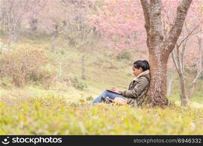 Asian girl using a laptop under tree. Asian girl using a laptop under cherry blossoms tree , The work is always with you.