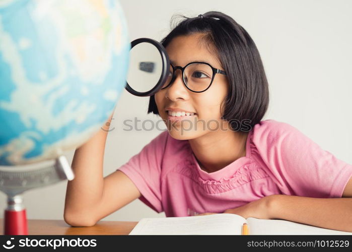 Asian girl wearing glasses is smiling and using a magnifying glass in the classroom, Educational concept