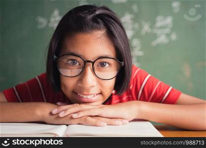 Asian girl with glasses is smiling and reading a book in class on blackboard