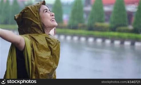 asian girl with positive face expression on the pouring rain day, standing on the road side wearing yellow raincoat soaking wet in the rain, its rainy season in Asia, enjoying her day with rain