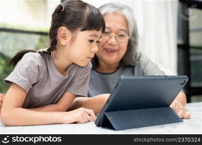Asian Grandmother with her two grandchildren having fun and playing education games online with a digital tablet at home in the living room. Concept of online education and caring from parents.