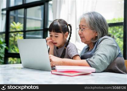 Asian Grandmother with her two grandchildren having fun and playing education games online with a computer notebook at home in the living room. Concept of online education and caring from parents.
