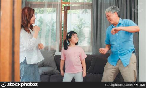 Asian grandparents and granddaughter listen to music and dance together at home. Senior Chinese, grandpa and grandma happy spend family time relax with young girl in living room concept.