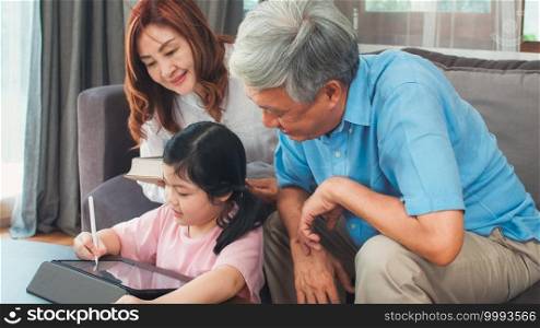 Asian grandparents and granddaughter video call at home. Senior Chinese, grandpa and grandma happy with girl using mobile phone video call talking with dad and mom lying in living room at home.
