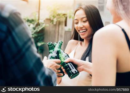 Asian group enjoying toasting drinks party with clinking beer bottle.