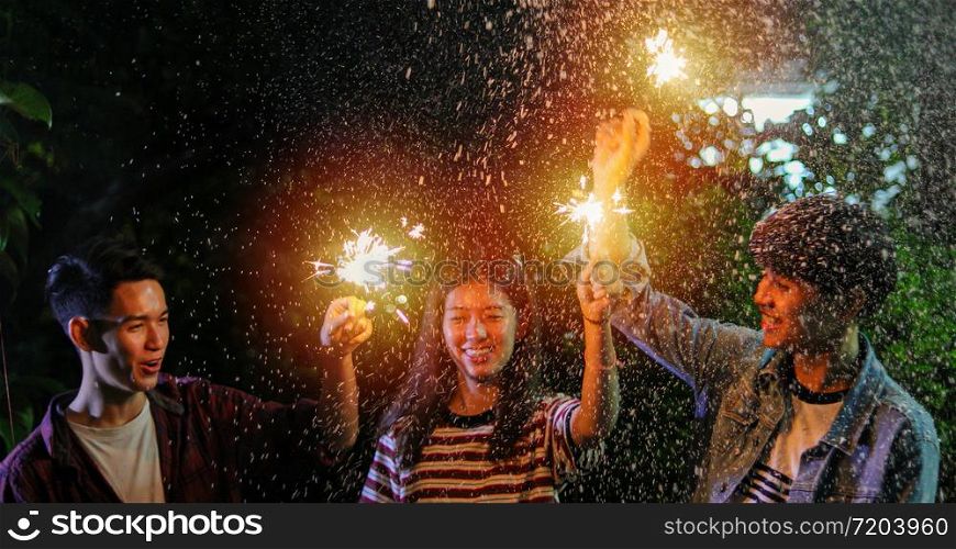 Asian group of friends having outdoor garden barbecue laughing with alcoholic beer drinks and showing group of friends having fun with sparklers on night