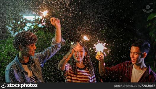 Asian group of friends having outdoor garden barbecue laughing with alcoholic beer drinks and showing group of friends having fun with sparklers on night