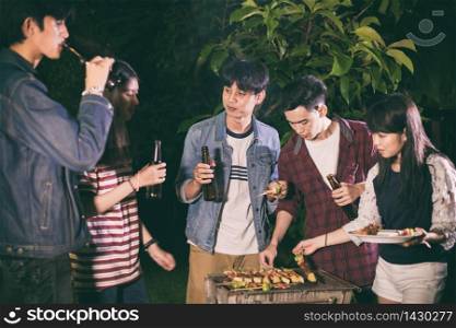 Asian group of friends having outdoor garden barbecue laughing with alcoholic beer drinks on night
