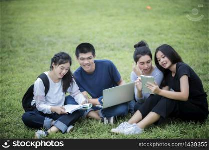 Asian Group of students using tablet and notebook sharing with the ideas for working on the campus lawn