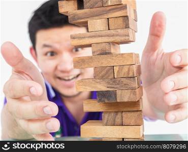 Asian guy is playing jenga, a wood blocks tower game for practicing physical and mental skill