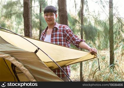 Asian handsome man wearing check shirt and pitching tent while camping in forest on summer time. Travel and backpacker concept.