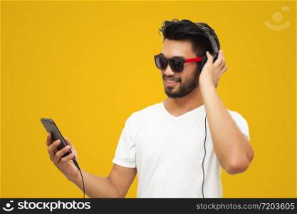 Asian handsome man with a mustache, smiling and laughing and using smart phone to listen music with headphones on yellow backgound