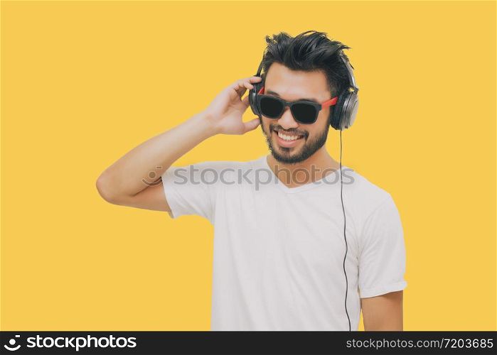 Asian handsome man with a mustache, smiling and laughing and using smart phone to listen music with headphones on yellow background