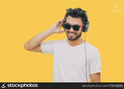 Asian handsome man with a mustache, smiling and laughing and using smart phone to listen music with headphones on yellow background
