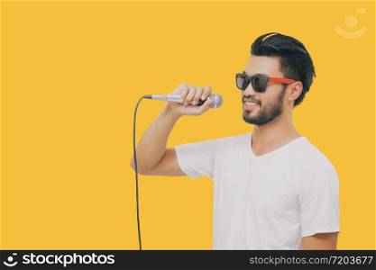 Asian handsome man with a mustache, smiling and singing to the microphone isolated on yellow background