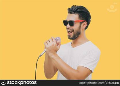 Asian handsome man with a mustache, smiling and singing to the microphone isolated on yellow background