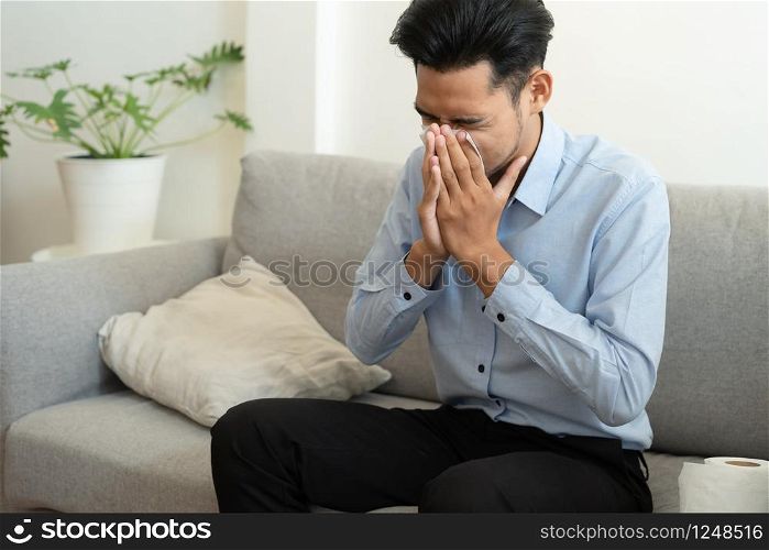 Asian handsome of man having flu season and sneeze using paper tissues sitting on a sofa at home, Health and illness concepts