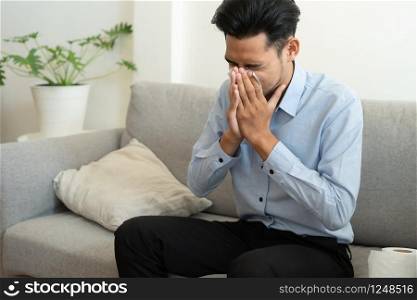 Asian handsome of man having flu season and sneeze using paper tissues sitting on a sofa at home, Health and illness concepts
