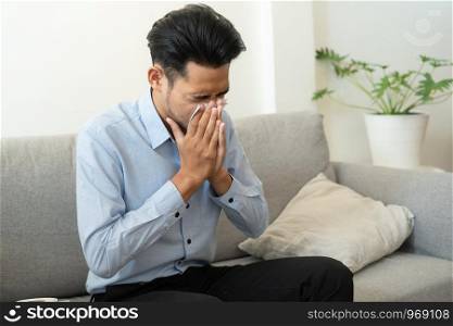 Asian handsome of man having flu season and sneeze using paper tissues sitting on sofa at home, Health and illness concepts