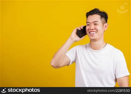 Asian handsome young man smiling positive talking on cellphone, lifestyle happy male using mobile smartphone studio shot isolated on yellow background