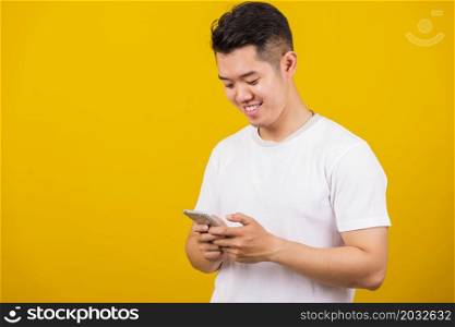 Asian handsome young man smiling positive using smartphone to get in touch screen or typing message, male reading good news message enjoy mobile application, studio shot isolated on yellow background
